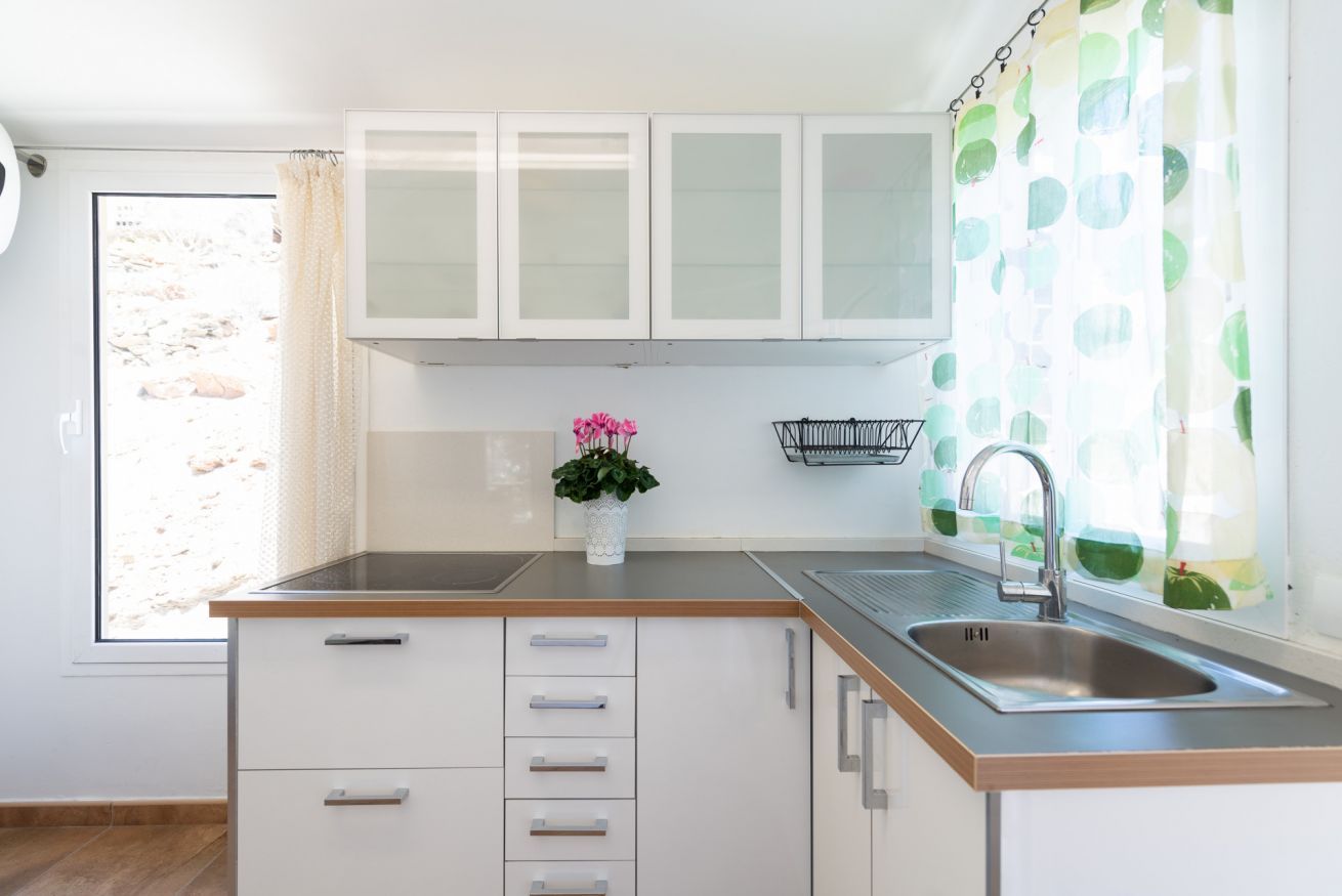 Una cocina con armarios blancos, encimera de madera, un fregadero y una ventana con vistas a rocas.