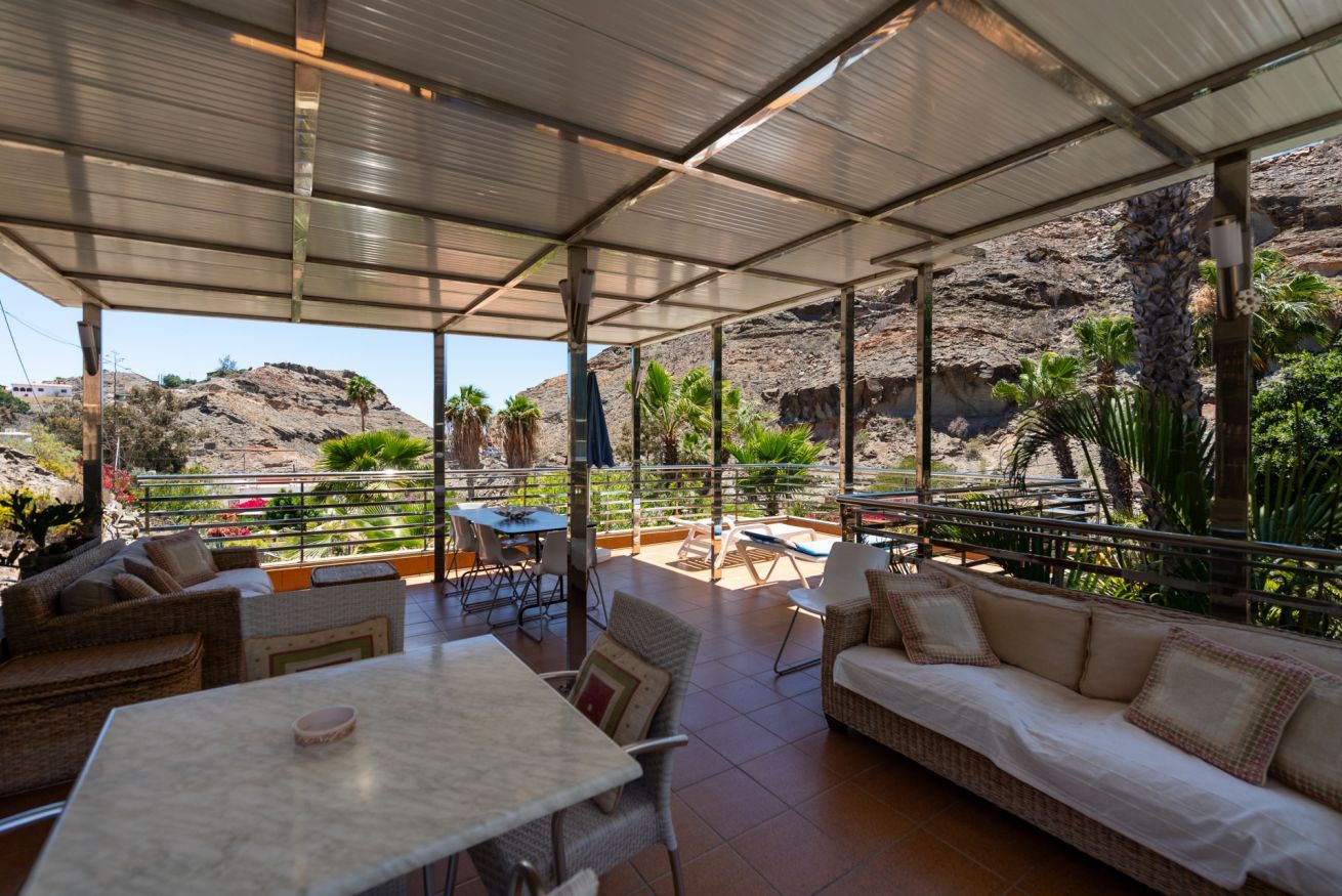 Un patio exterior con asientos y mesas, con vistas a un paisaje rocoso y vegetación.