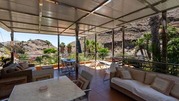Un patio exterior con asientos y mesas, con vistas a un paisaje rocoso y vegetación.