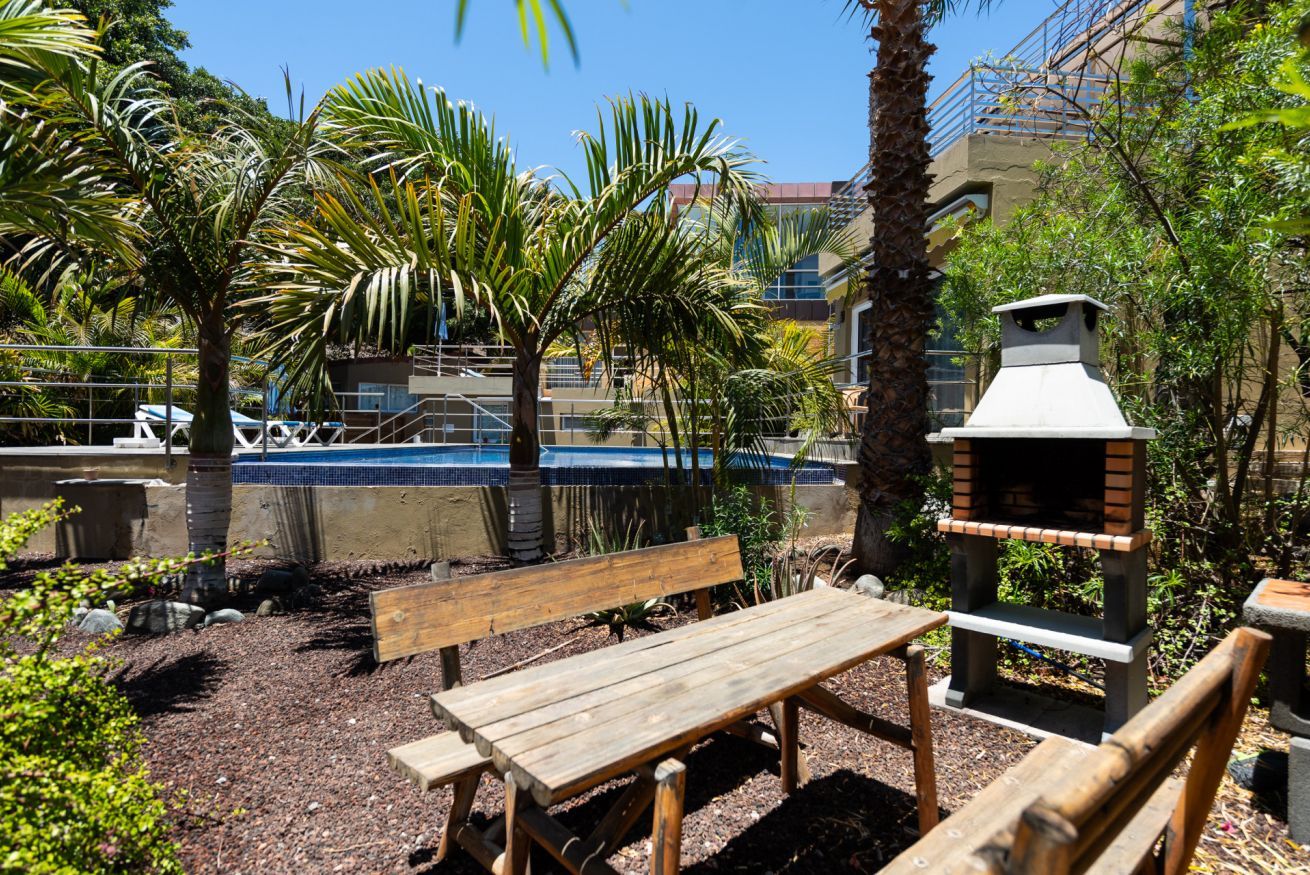 Un área de patio al aire libre con un banco de madera, una parrilla y una piscina de fondo.