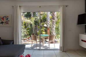 Una habitación con puerta de vidrio corredera que da a un patio con dos sillas de mimbre y una mesa pequeña.