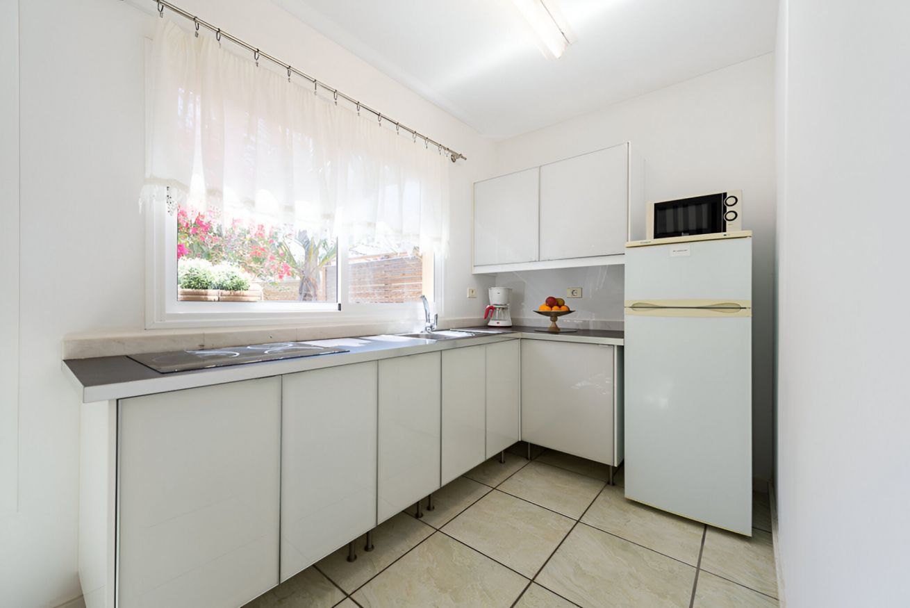 Una cocina con armarios blancos, microondas, refrigerador y ventana con vista a un jardín.