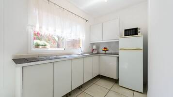 Una cocina con armarios blancos, microondas, refrigerador y ventana con vista a un jardín.