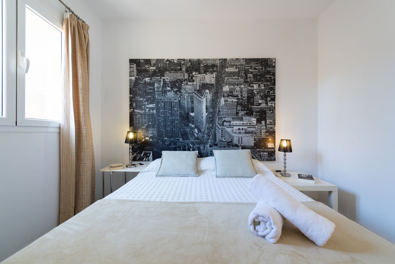 Een hotelkamer met een groot bed, twee nachtkastjes, een stadsgezicht aan de muur en een raam met gordijnen.