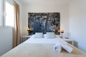 Habitación de hotel con una cama grande, dos mesitas de noche, un cuadro con vista a la ciudad y una ventana con cortinas.