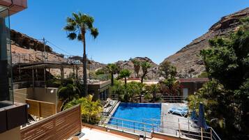 Un área de piscina con una piscina azul cristalina, rodeada de palmeras y un telón de fondo montañoso.