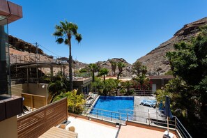 Ett poolområde med en klarblå pool, omgivet av palmer och en bergig bakgrund.