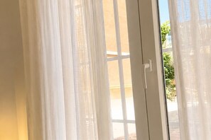 A view through a window with sheer white curtains, a white door, and a glimpse of greenery outside. - Pet-Friendly Stay in Madrid (Madrid)