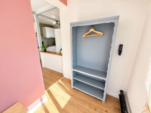 Ein Zimmer mit Holzboden, einem grauen Kleiderschrank mit Regalen und einer Kleiderstange.