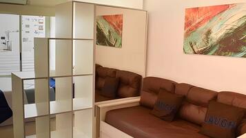 Una sala de estar moderna con un sofá de cuero marrón, un armario blanco y pinturas abstractas en la pared.