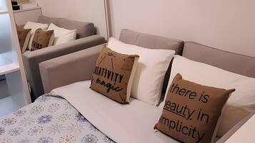 A hotel room with a bed, two sofas, and a small table. There are pillows with text on them.