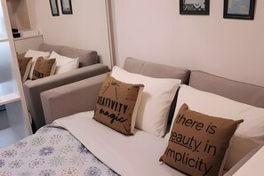 Ein Hotelzimmer mit einem Bett, zwei Sofas und einem kleinen Tisch. Die Kissen haben Aufschriften.