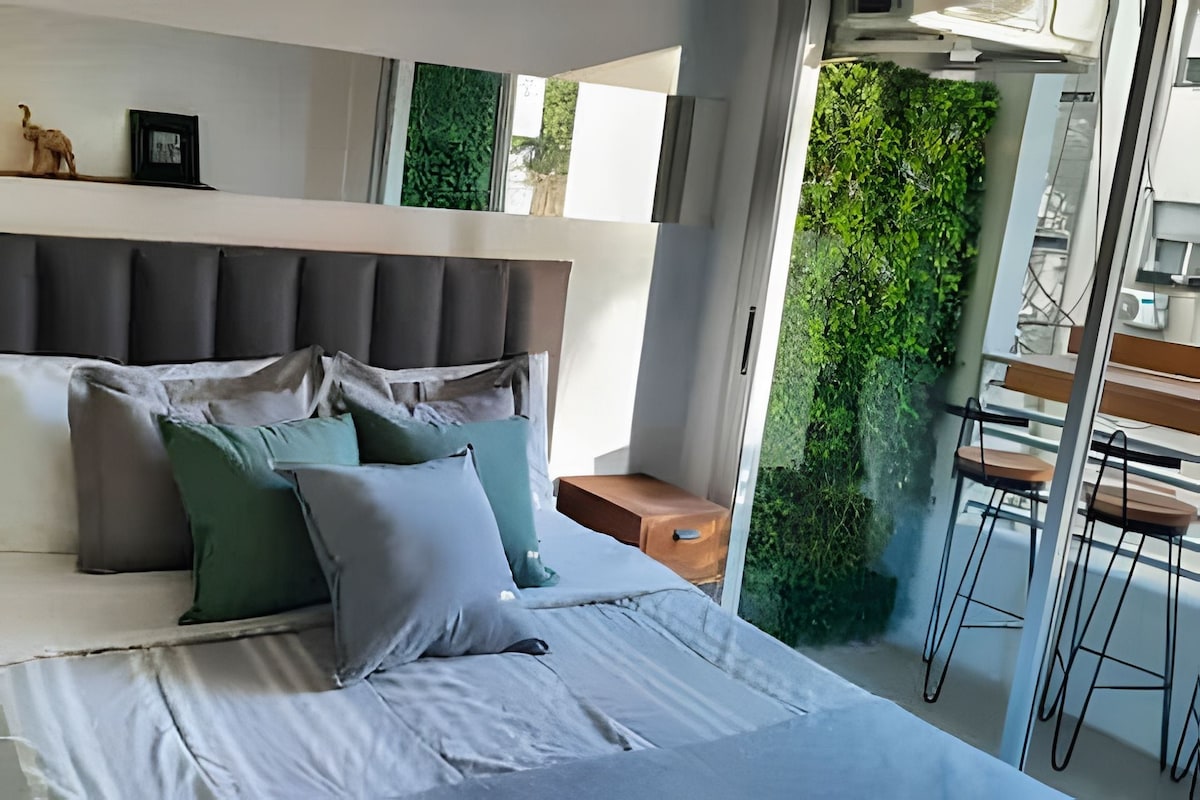 Un dormitorio moderno con una cama grande, un cabecero y vistas a un balcón con vegetación.