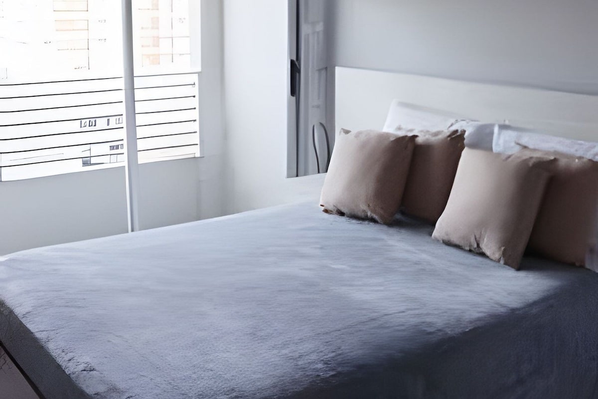 Un dormitorio con una cama grande, una lámpara colgante, una ventana con persianas y una obra de arte en la pared.