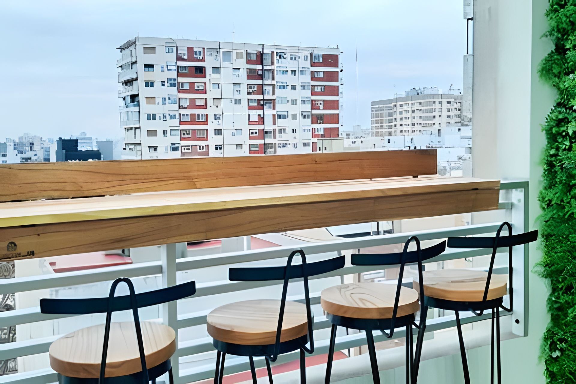 Un balcón con una mesa de madera y cuatro sillas, con vista a un paisaje urbano con edificios de varios pisos.