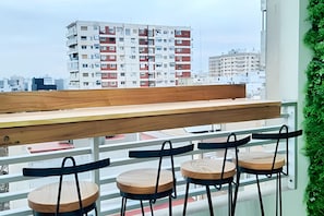 Un balcón con una mesa de madera y cuatro sillas, con vista a un paisaje urbano con edificios de varios pisos.