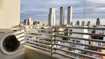 Un balcón con lavadora, con vistas a un paisaje urbano con varios edificios altos.