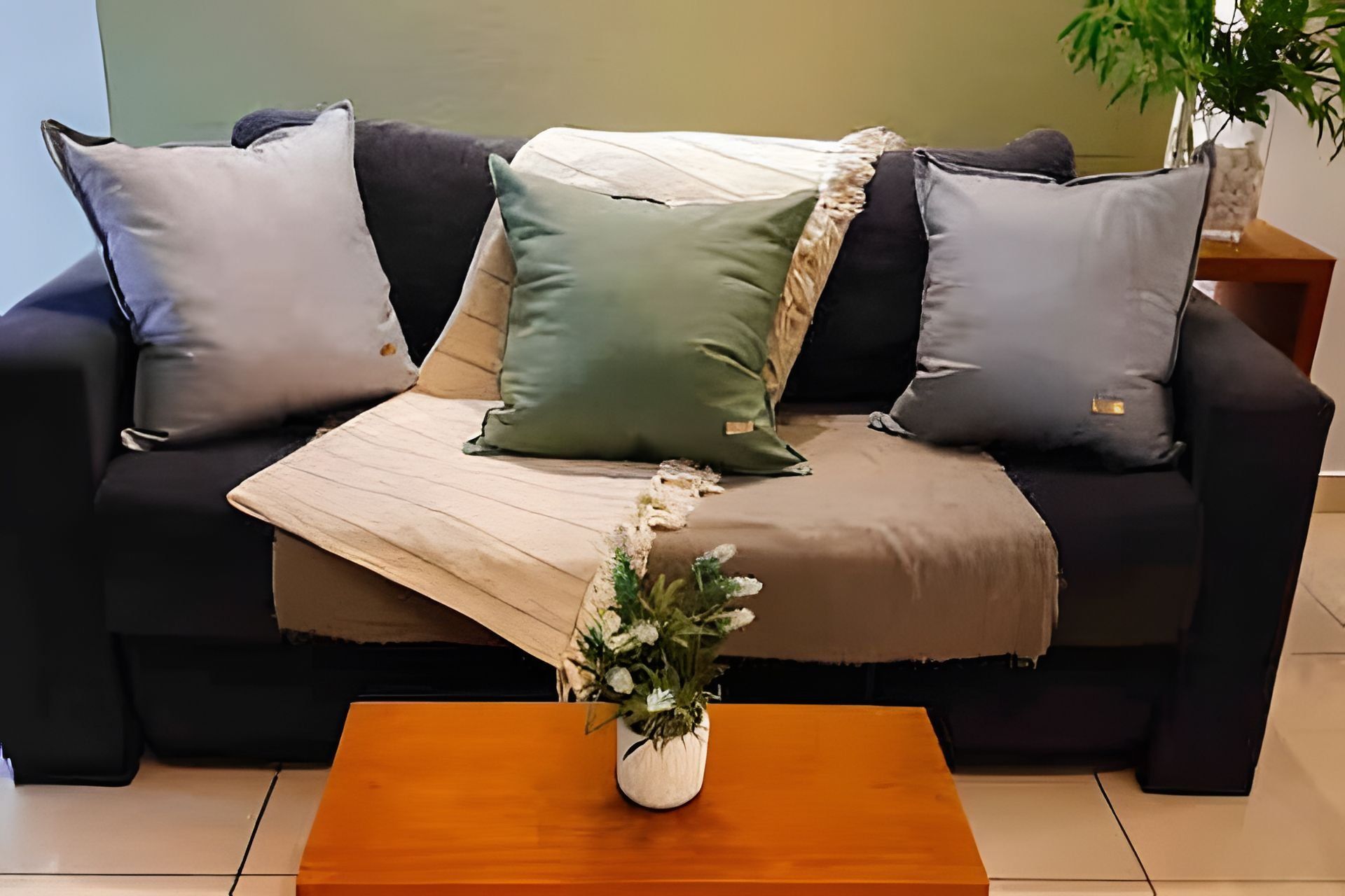 Una sala de estar con sofá, cojines, una mesa de centro de madera y un florero con flores.