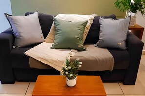Ein Wohnzimmer mit einer Couch, Kissen, einem Holztisch und einer Vase mit Blumen.