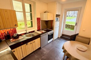 Une cuisine compacte équipée d’un évier, d’une cuisinière et d’un réfrigérateur, avec des armoires en bois et une vue sur l’extérieur.