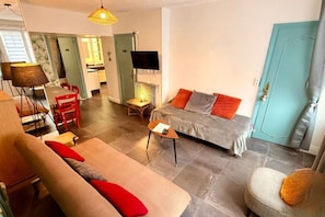 Ein Wohnzimmer mit einer Couch, einem Esstisch mit Stühlen, einem Fernseher und einer Tür.