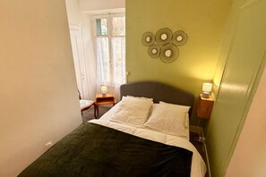 Ein Schlafzimmer mit einem Bett, einem Nachttisch, einer Wandlampe und einem Fenster mit Vorhängen.