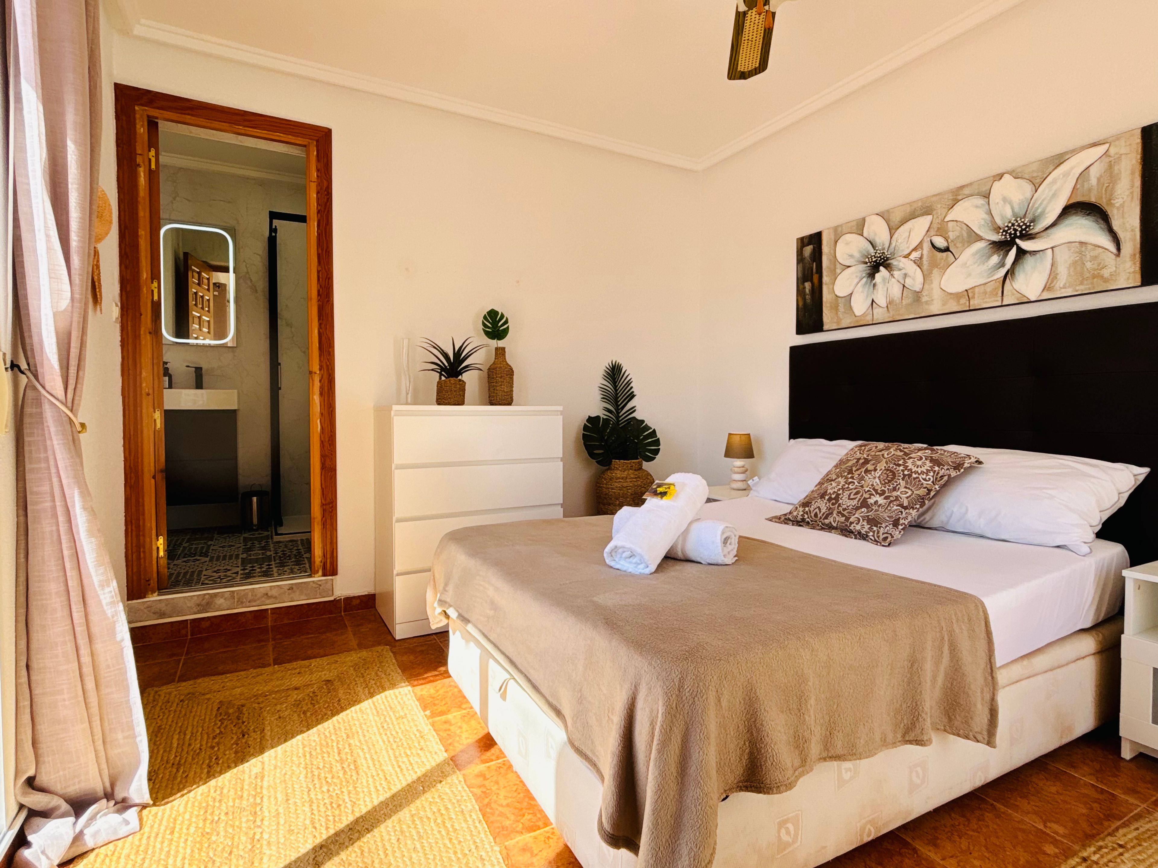 A bedroom with a bed, bedside tables, a mirror, a painting, and a door leading to a bathroom.