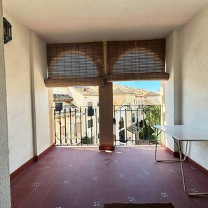 A balcony with a tiled floor, a metal table, and a view of buildings through a metal gate. - Casa Nalon 2 by Rental Hero (Alcazares, Los)