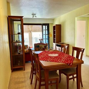 A dining area with a wooden table and chairs, a red table runner, and a glass cabinet with items on display. - Casa Nalon 2 by Rental Hero (Alcazares, Los)