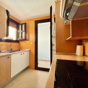 A kitchen with a built-in microwave, a sink, and a window with curtains. - Casa Nalon 2 by Rental Hero (Alcazares, Los)