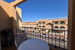 A balcony with a table and chairs, a grill, and a view of multi-story buildings with balconies. - Casa Playa by Rental Hero (Alcazares, Los)
