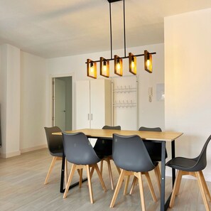 Un comedor con una mesa de madera y seis sillas, un moderno colgante de luz y un perchero con ganchos.