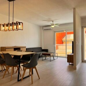 Un comedor con mesa y sillas de madera, un ventilador de techo y vistas a un balcón con paredes anaranjadas.