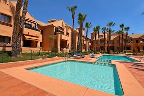 A resort with multiple swimming pools, palm trees, and a clear blue sky. - Casa Ribera Beach by Rental Hero (Narejos, Los)