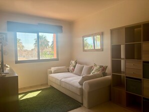 A room with a sofa, a small table, a desk, a green rug, and a built-in wooden cabinet. - Casa Ribera Beach by Rental Hero (Narejos, Los)