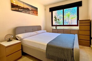 A bedroom with a bed, bedside table, lamp, window, and a view of greenery outside. - Casa Ribera Beach by Rental Hero (Narejos, Los)