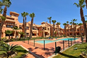 A resort with multiple-story buildings, a swimming pool, and palm trees. - Casa Ribera Beach by Rental Hero (Narejos, Los)