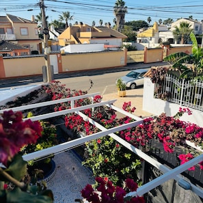A residential area with a white fence, red flowers, and a car parked on the street. - Casa de Los Angeles by Rental Hero (Alcazares, Los)
