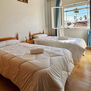 Une chambre d’hôtel avec deux lits, une fenêtre avec des rideaux et une vue sur les palmiers à l’extérieur.