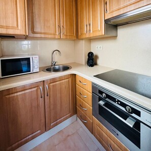 A compact kitchen with wooden cabinets, a microwave, a sink, a coffee maker, and a stove. - Casa de Los Angeles by Rental Hero (Alcazares, Los)