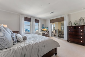 Ein Schlafzimmer mit einem großen Bett, einem Schminktisch, einem Schreibtisch mit Computer und Blick aufs Meer.