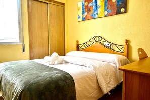 A neatly made bed with a patterned bedspread and pillows, a wooden headboard, a wooden nightstand, and a colorful abstract painting on the wall. - Casa Los Narejos Beach by Rental Hero (Alcazares, Los)