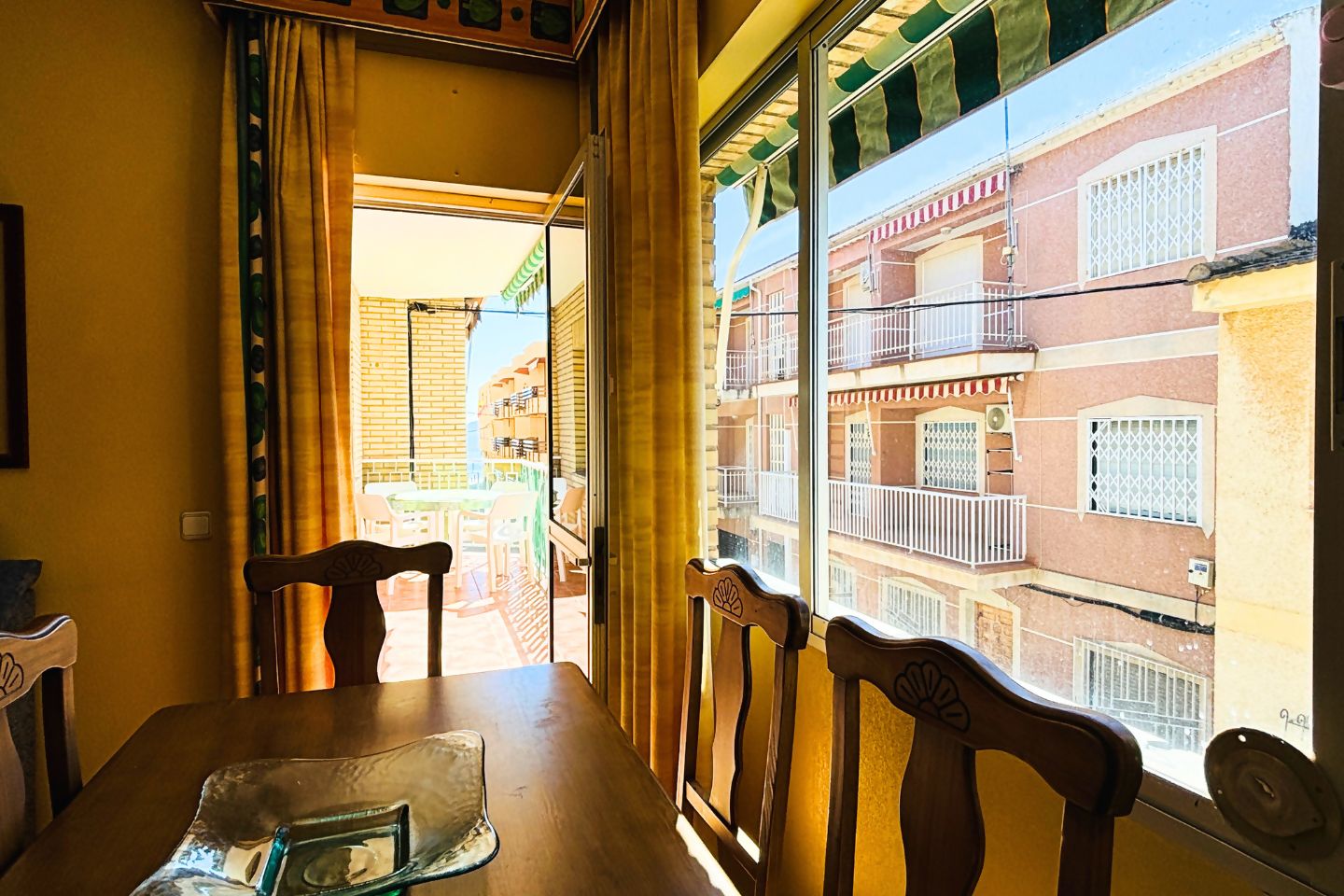 A room with a table and chairs, a window with a view of a building with balconies.