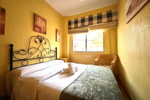 A room with a bed, a window with a checkered blind, a chair, and artwork on the walls. - Casa Los Narejos Beach by Rental Hero (Alcazares, Los)