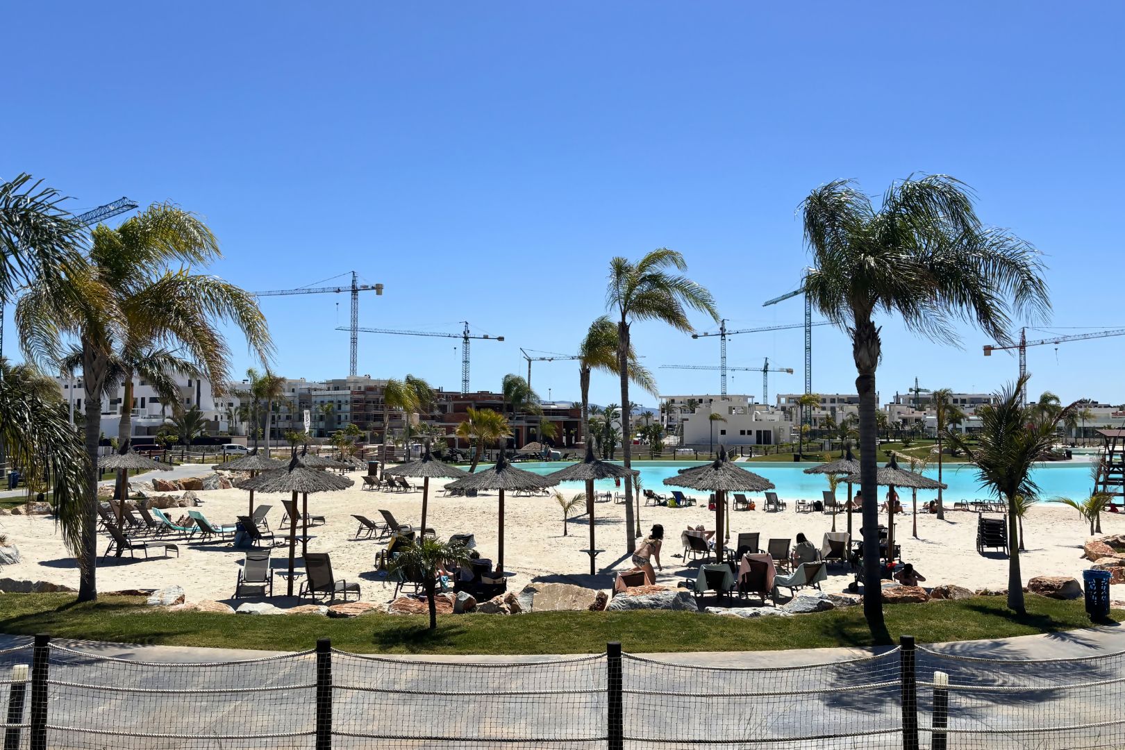 Un complejo turístico en la playa con piscina, tumbonas y palmeras.