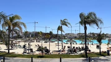 Un complejo turístico en la playa con piscina, tumbonas y palmeras.
