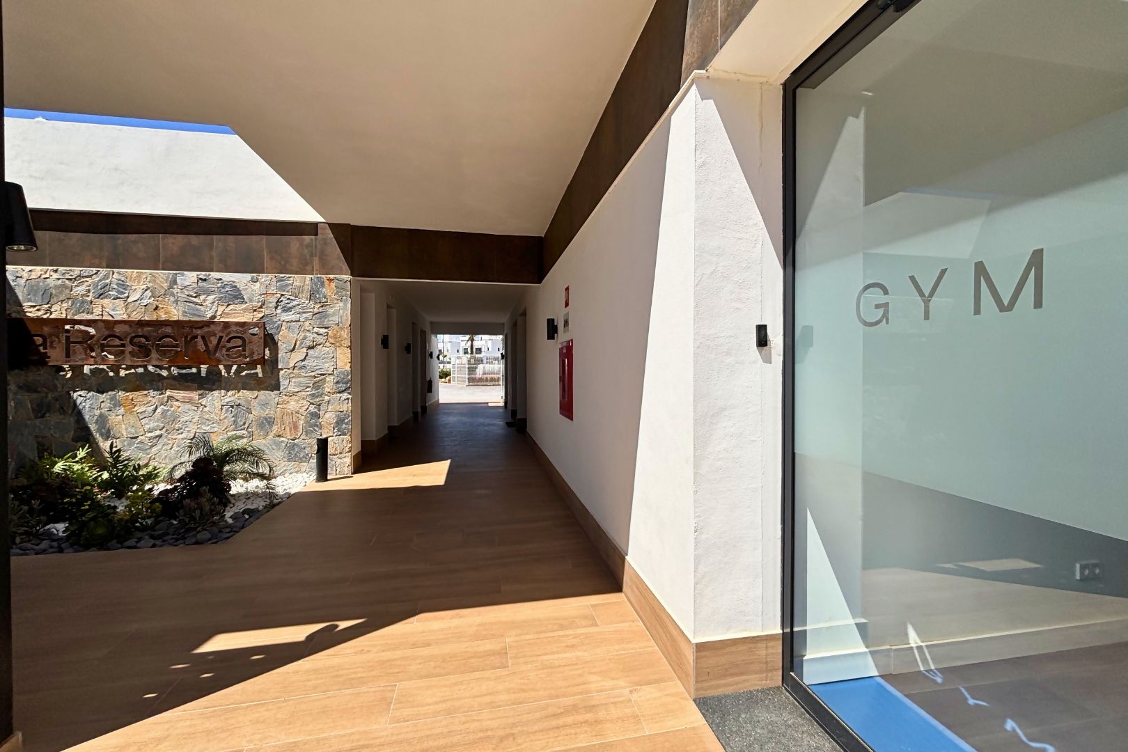Un couloir d’hôtel avec un mur en pierre, un plancher en bois et une porte en verre portant l’inscription « SALLE DE SPORT ».