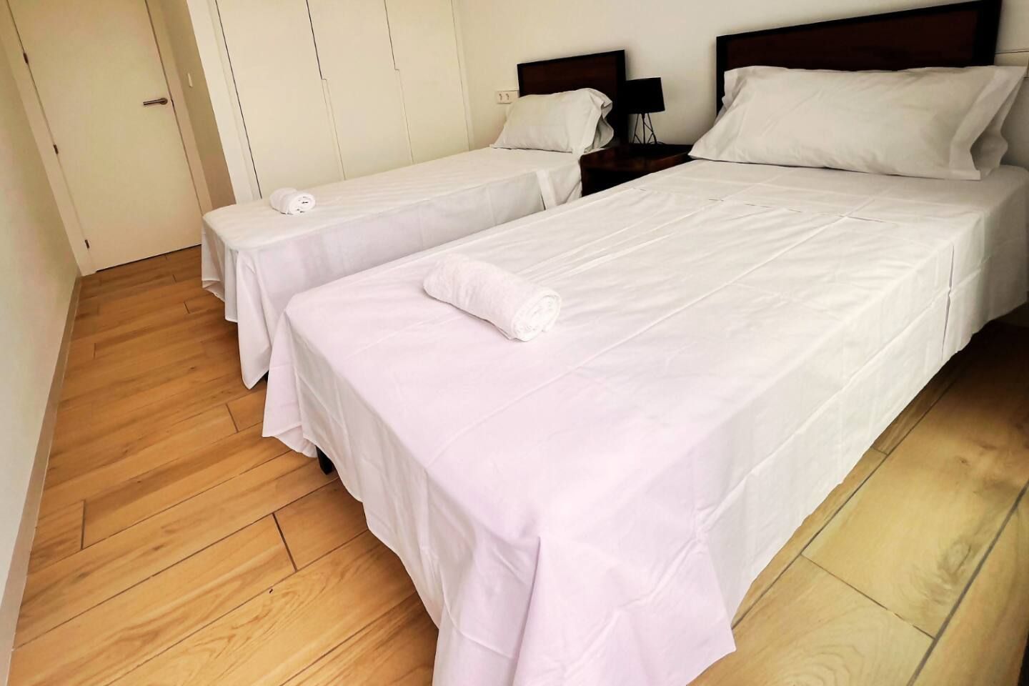 Una camera d'albergo con due letti singoli, pavimento in legno e una porta bianca.