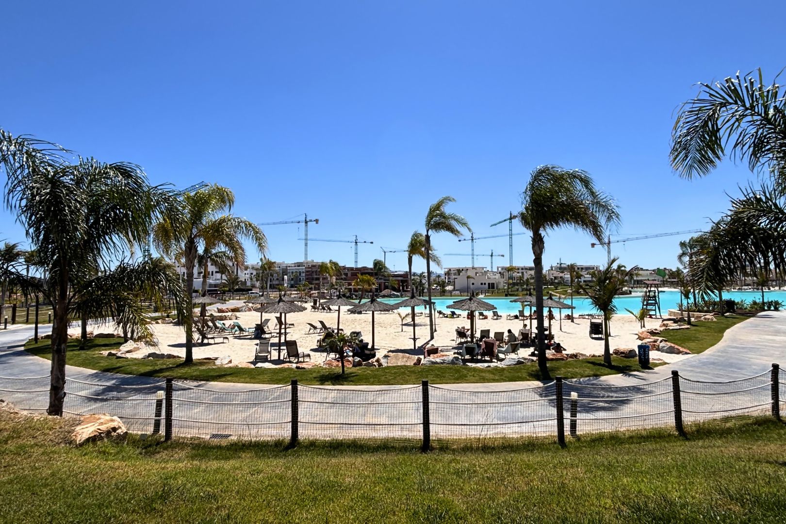A beach area with lounge chairs, umbrellas, and a pool.