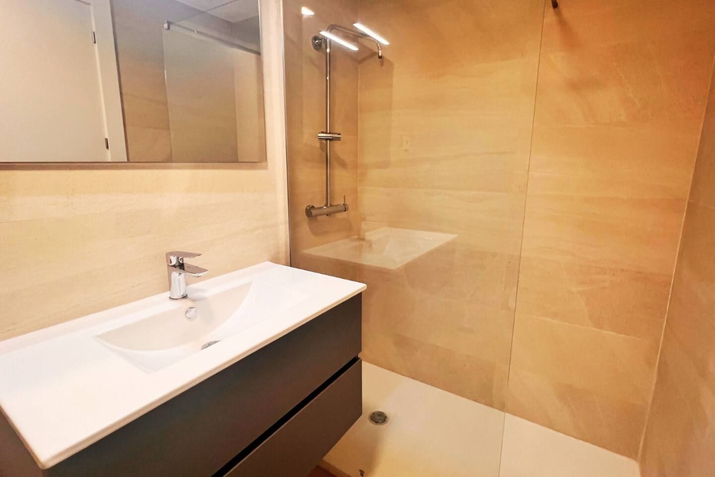 Un baño con lavamanos blanco, espejo y ducha.